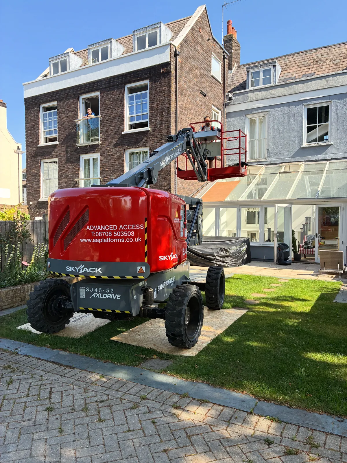 Cherry picker in use to reach a boiler flue above a glass roof in Hampton